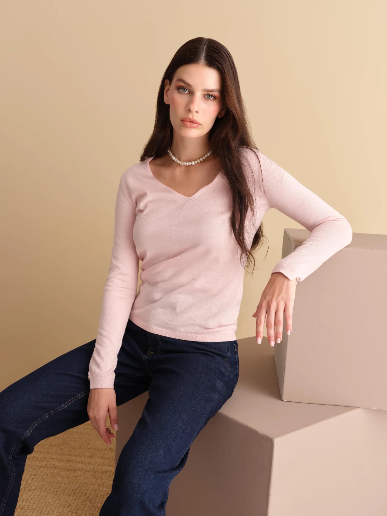 Pembe kazak ve kot pantolonlu model, bej fonda oturuyor